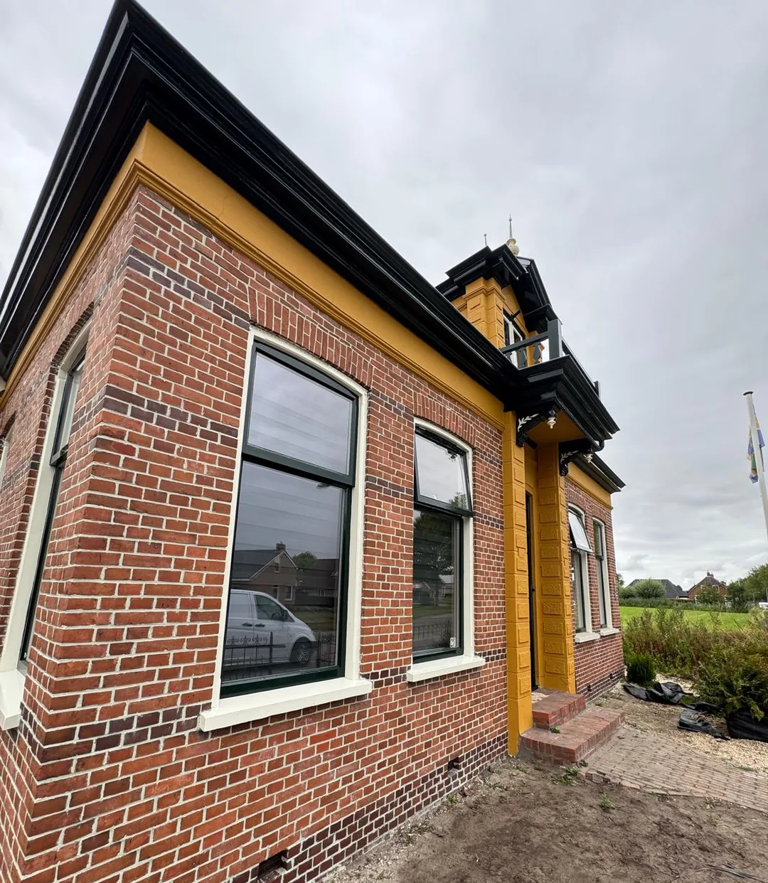 Zijgevel van een vrijstaand huis in Usquert met donkergroen gelakte ramen, gebroken witte vensterbanken en een zwarte daklijst